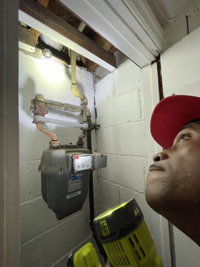 Chad inspecting gas meter and plumbing in a basement with a professional flashlight
